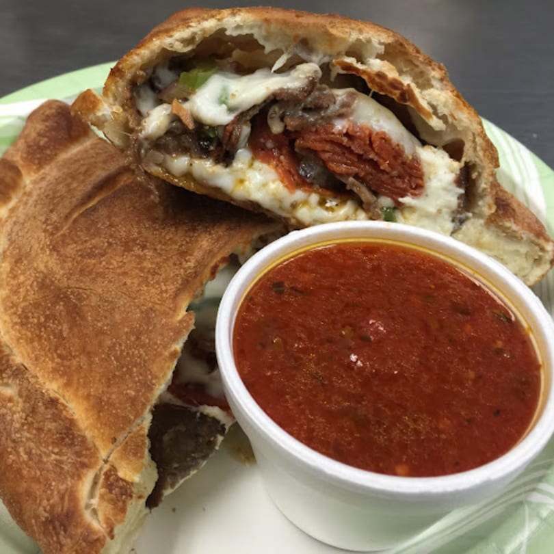 A calzone, cut open to reveal melted cheese, pepperoni, and other fillings, with a side of marinara sauce.