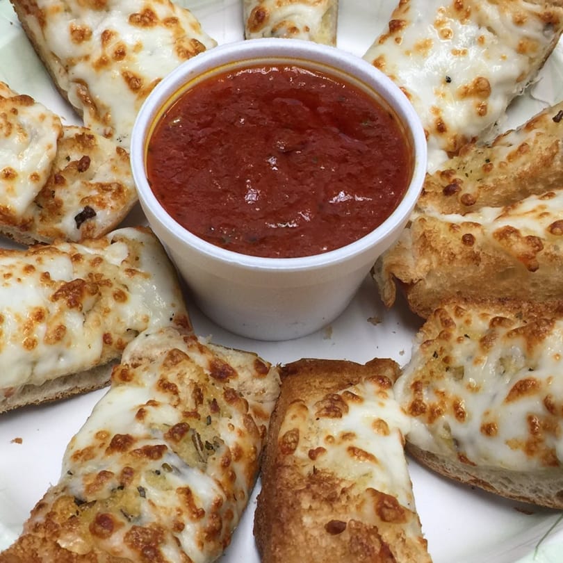 Cheesy garlic breadsticks with melted mozzarella and golden crust, surrounding a cup of marinara sauce.