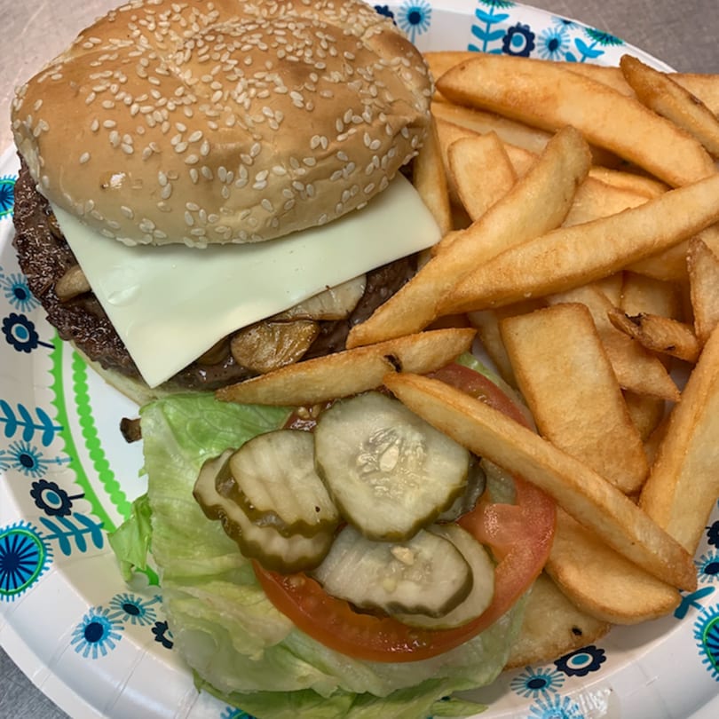 A cheeseburger with lettuce, tomato, pickles, and fries on a patterned paper plate.