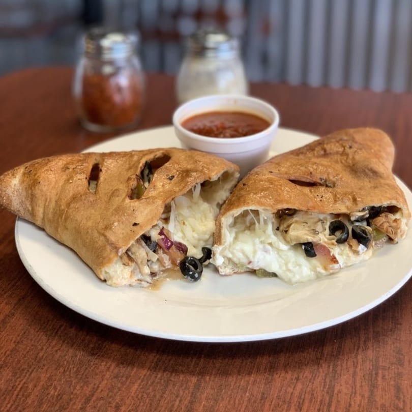 A calzone from Pizza And Grill, cut in half, revealing melted cheese, chicken, and olives.